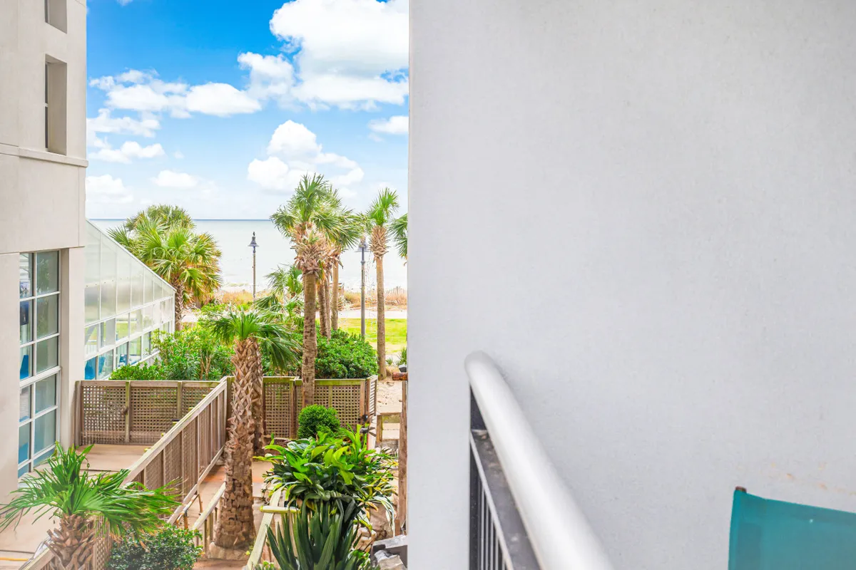 This serene scene captures a balcony perspective overlooking palm trees and the ocean beyond. The view is open and tranquil, with the balcony railing framing a natural, breezy setting ideal for unwinding or greeting the sunrise.