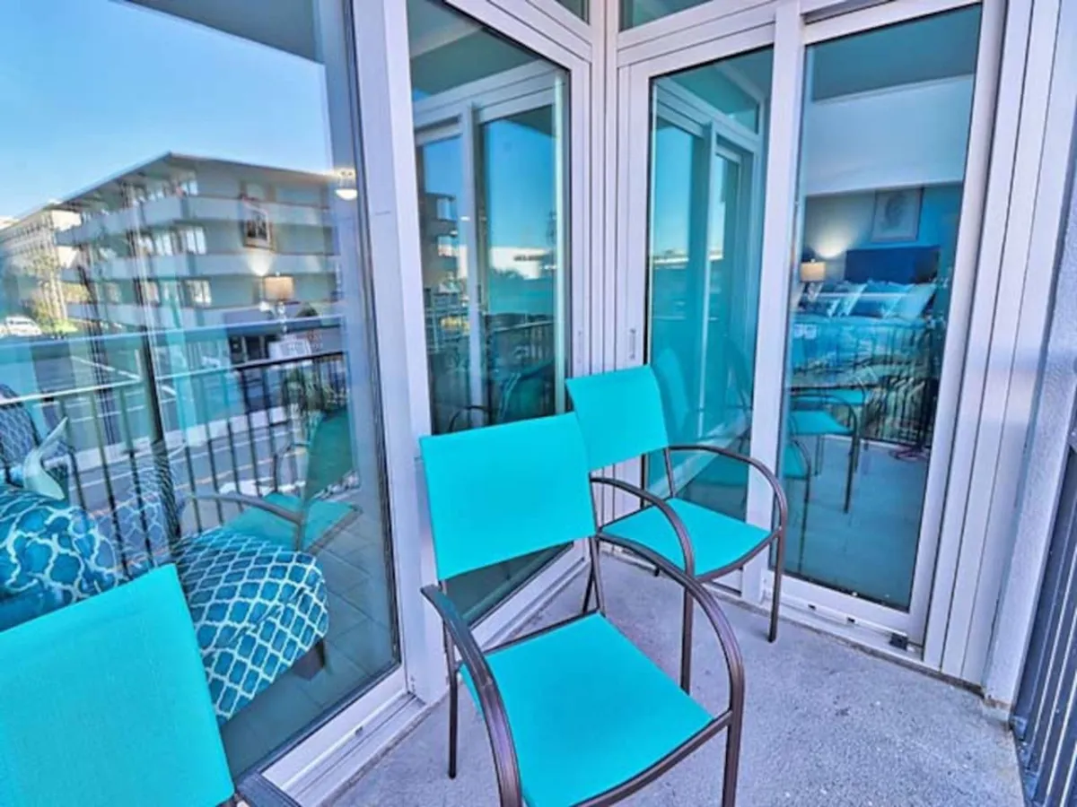 This image features turquoise chairs on a balcony just outside glass doors, with glimpses of stylish interior decor visible through the glass. The scene evokes a sense of winding down after a night out, hosting friends for drinks, or simply enjoying the evening air while connected to the energy of the city.