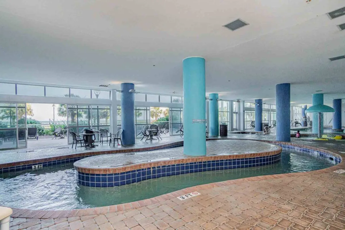 A lively pool area within the resort, featuring blue columns, plenty of seating, and guests enjoying swimming and socializing. The space is designed for relaxation and fun, ideal for groups looking to spend quality time together.