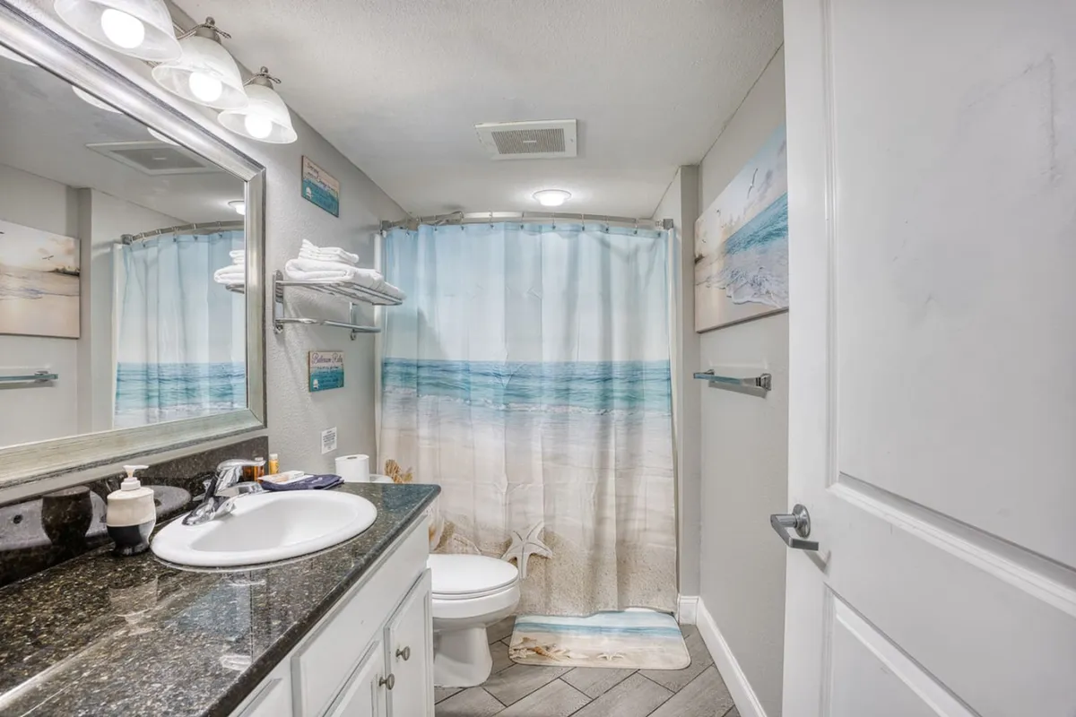A sleek, serene bathroom with a modern vanity, large mirror, chic sink, and decorative art. Subtle lighting and a shower curtain evoke a bright, refreshing atmosphere, perfect for private moments of rejuvenation.