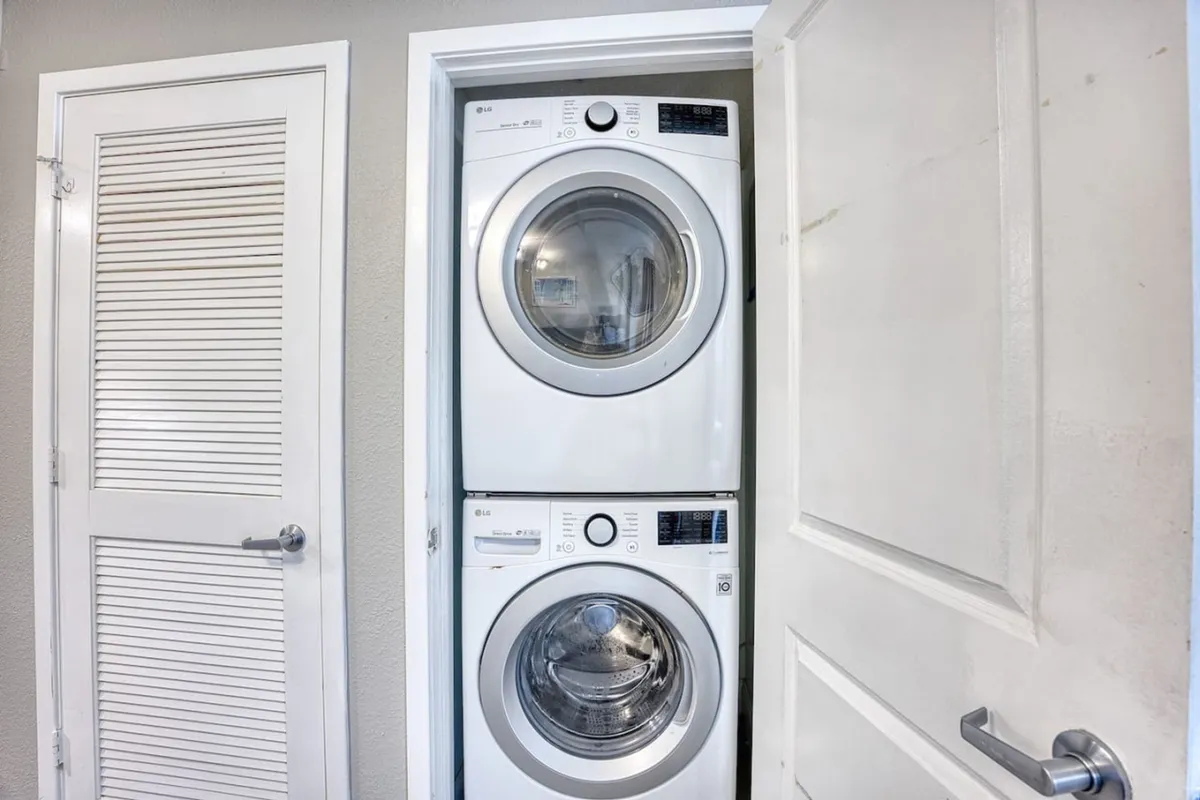 The image displays a compact laundry space with a stacked washer and dryer set neatly into a white closet, highlighting organizational efficiency within the home.