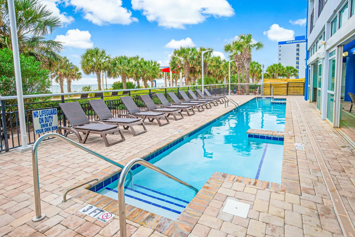 An inviting outdoor pool surrounded by lounge chairs and palm trees, with signage indicating a family-friendly atmosphere. The scene suggests leisurely swims, sunbathing, and poolside gatherings under the sun, all within the resort's welcoming space.