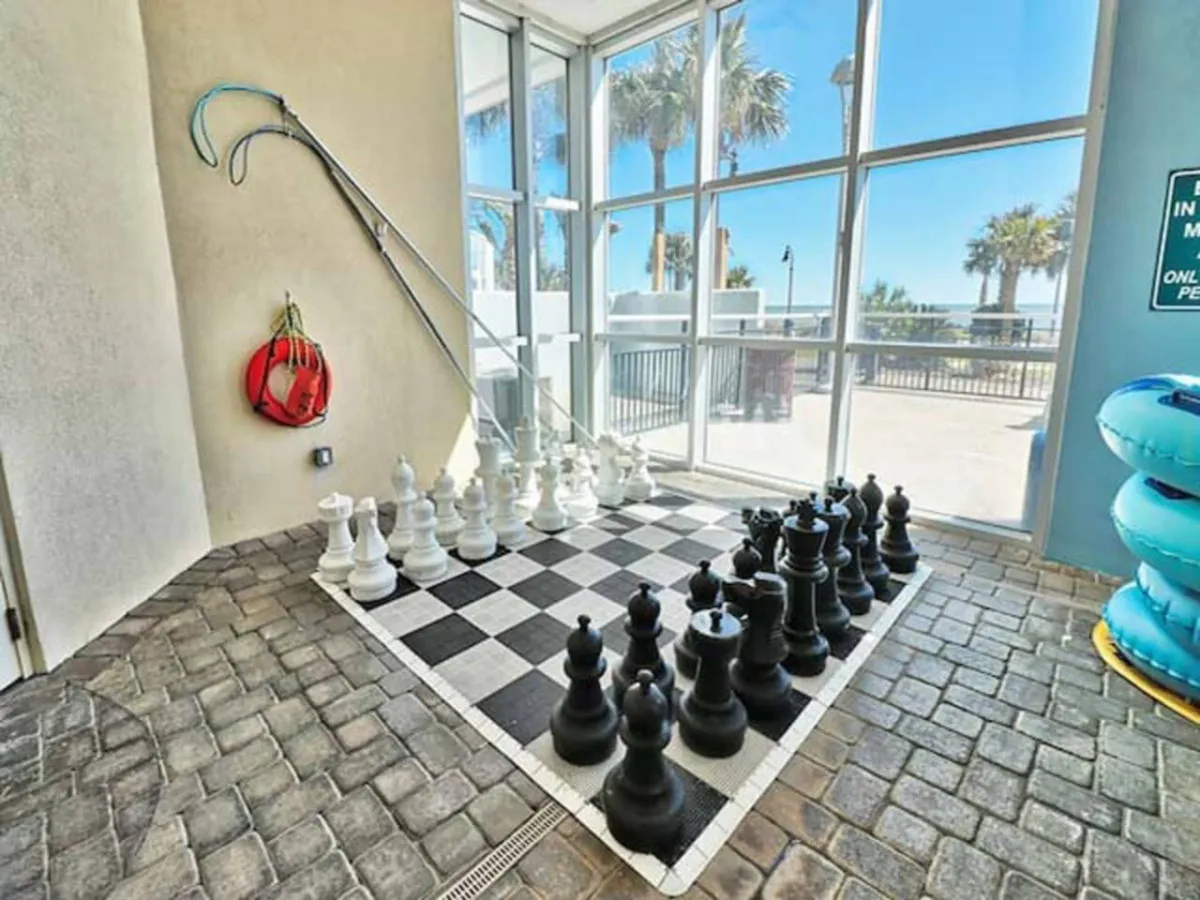 A playful communal outdoor recreation area with a large chessboard, colorful pool floats, and spaces for socializing and casual gatherings. The scene conveys a lighthearted, social energy ideal for group activities.