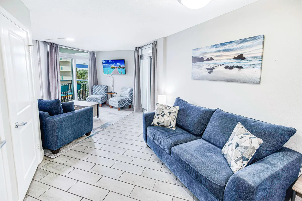 Another angle of the living room showing a sofa, armchairs, a television, and wall artwork. The setup highlights ample seating and a cozy environment for movie nights or socializing.